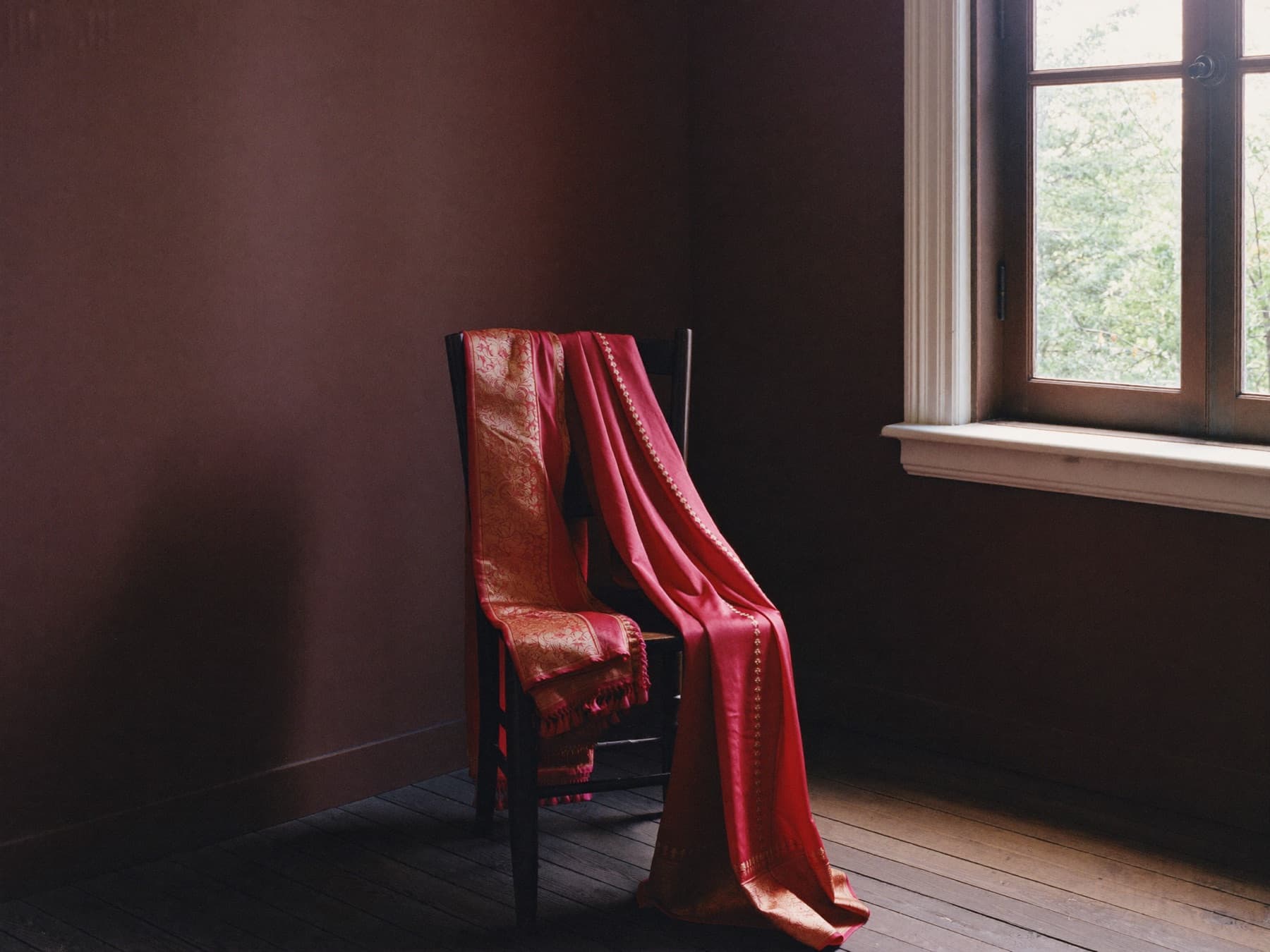 Crimson and gold silk cloth draped over a dark wooden chair in soft window light