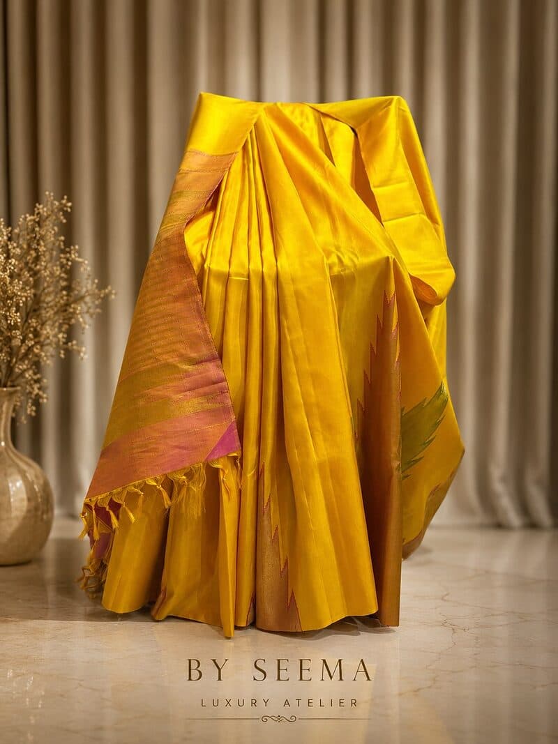A gold silk saree with a woven border, draped full length on a stand