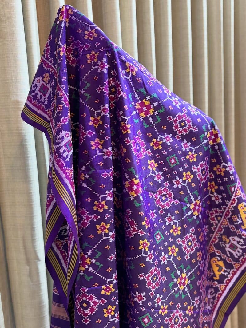 A purple patola dupatta with red and white ikat motifs, draped over a stand
