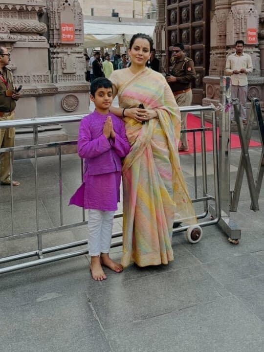 Kangana Ranaut wearing the rangkat saree outside a carved temple gateway, a child beside her