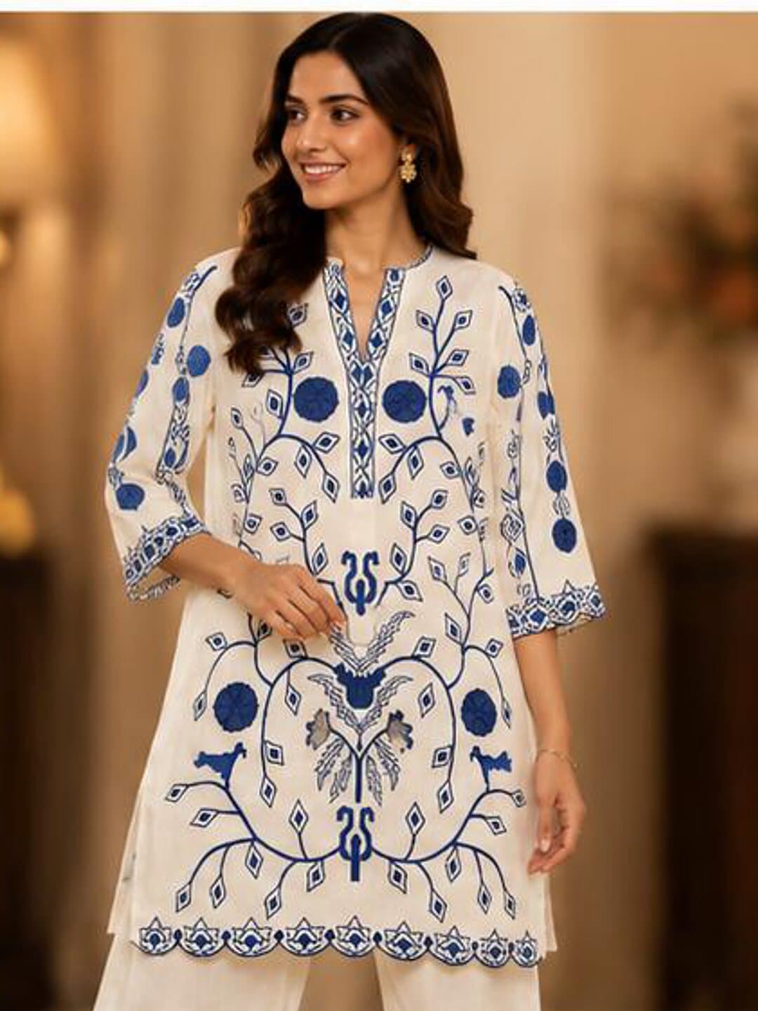 Ivory cotton kurta embroidered in blue with a climbing vine of leaves, blossom and small birds, above a scalloped hem